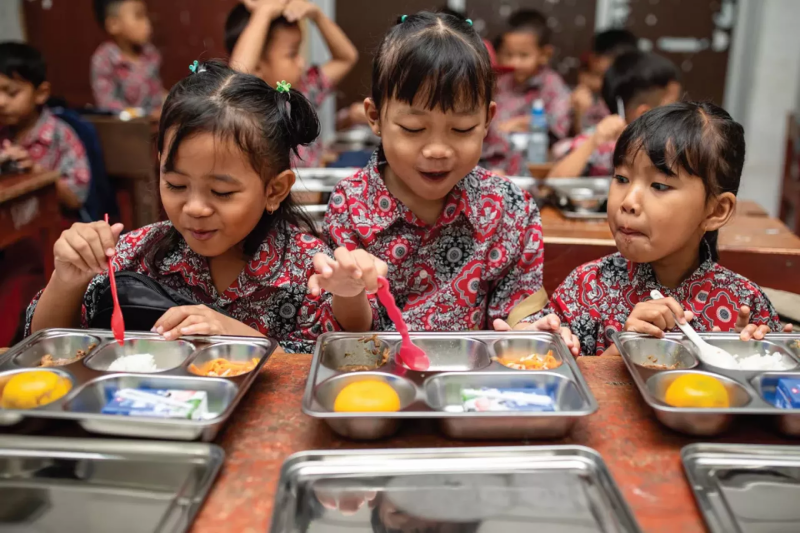 Anak sekolah menerima makanan bergizi gratis di kantin sebagai simbol program MBG.